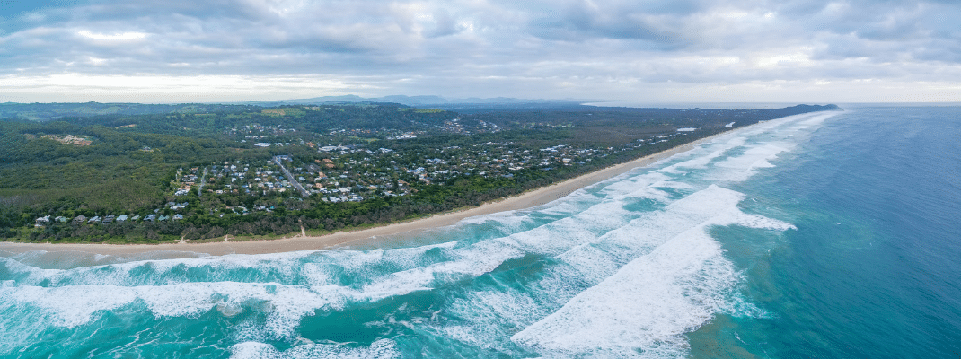 Aerial panorama of Suffolk Park suburb and ocean beach under moody sky. New South Wales, Australia