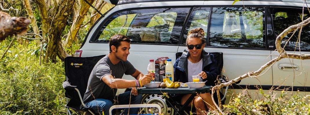 Young couple having breakfast next to their hired station wagon