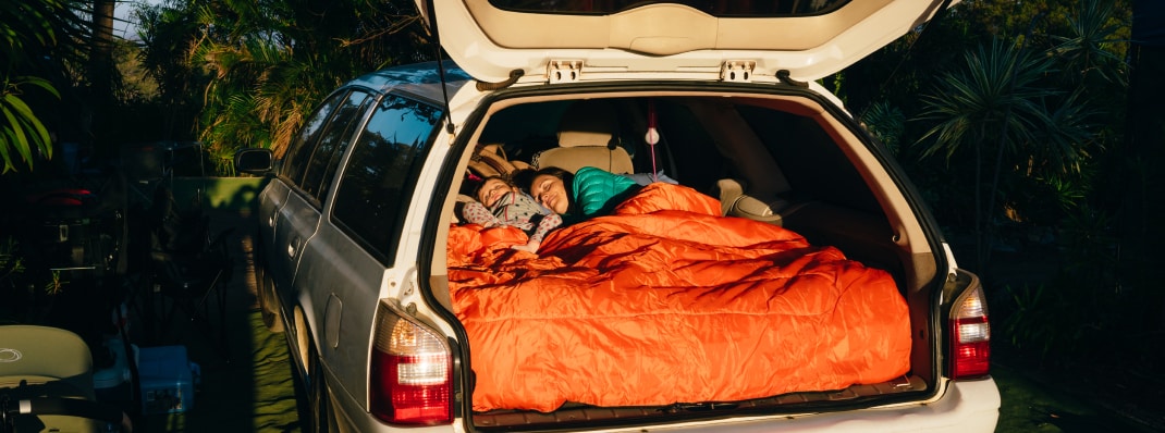 A mother and child sleeping in the back of a rented station wagon