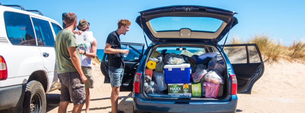 A group of three friends camping beachside in a packed station wagon